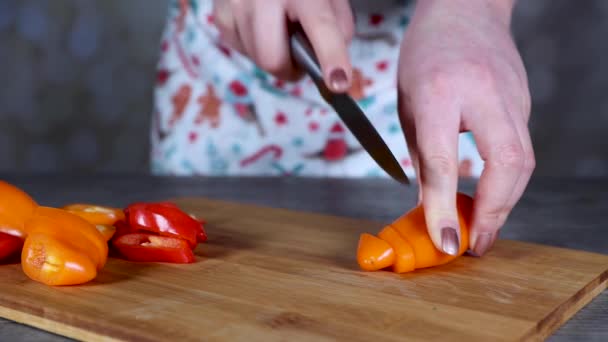 Una mujer en una cocina cortando pimientos anaranjados y rojos en una tabla de cortar madera concepto de cocina casera - Metraje, vídeo