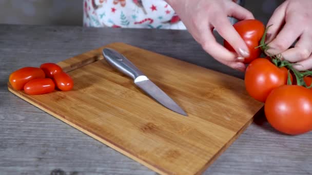 Una mujer en una cocina cortando un tomate rojo grande en una tabla de cortar, concepto de cocina casera - Metraje, vídeo