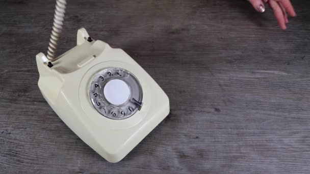 Een elegante vrouw de hand oppakken, neerzetten en flirten op een oude vintage jaren 70 en 80 stijl roterende telefoon ontvanger op een houten achtergrond, retro kantoor telefoongesprek concept - Video