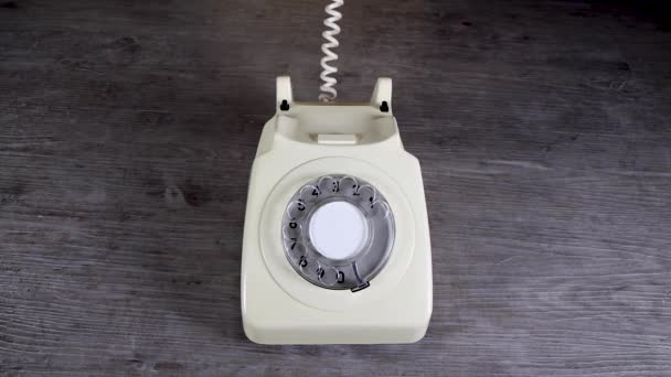Elegante mano de mujer recogiendo y poniendo un viejo vintage 70 y 80 estilo receptor de teléfono giratorio sobre un fondo de madera, concepto de llamada telefónica de oficina retro - Imágenes, Vídeo