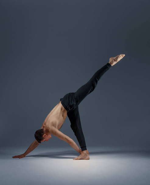 Męska joga utrzymuje równowagę na dłoniach, pozycji medytacji, szarym tle. Silny człowiek robi ćwiczenia joginowe, trening asana, najwyższa koncentracja, zdrowy styl życia - Zdjęcie, obraz