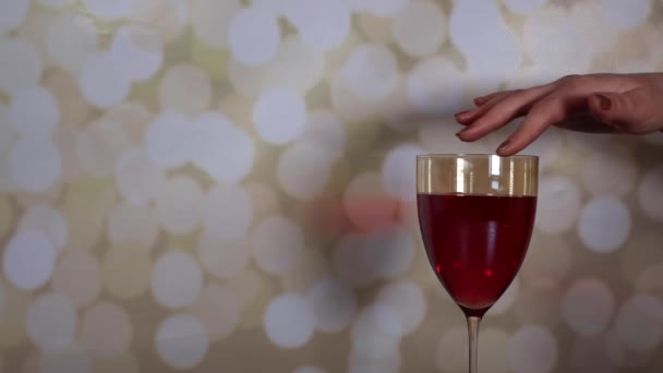 La mano de una mujer sosteniendo un vaso de vino de rosas y tocándolo seductor sobre un fondo brillante - Metraje, vídeo