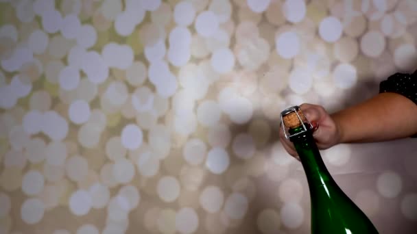 Láhev šampaňského se otvírá, vyskakuje a letí přes místnost, otevřena ženou s dlouhými lesklými nehty na třpytivém pozadí - Záběry, video
