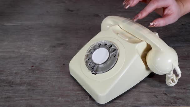 Elegante mano de mujer recogiendo y poniendo un viejo vintage 70 y 80 estilo receptor de teléfono giratorio sobre un fondo de madera, concepto de llamada telefónica de oficina retro - Imágenes, Vídeo