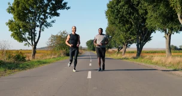 Veselý smíšené závody mladí sportovci přátelé běžci běží na silnici brzy ráno na venkově a mluví. Komunikace. Šťastní multietničtí sportovci v přírodě. - Záběry, video