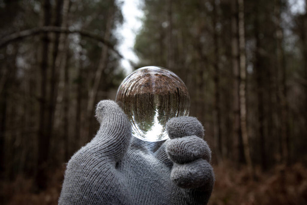 Lens Ball held by gloves hand in Czech forest on a grey day. Lensball optika tmavé dramatické venku - Fotografie, Obrázek