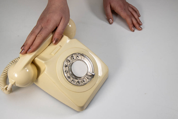 Un vecchio telefono retrò su sfondo bianco a cui risponde una donna elegante - Foto, immagini