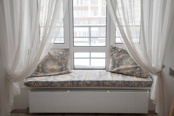 Een raam in de slaapkamer met gordijnen, een gezellig appartement, een plek om te ontspannen. - Foto, afbeelding