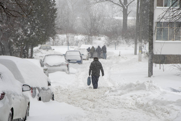 Hóval borított parkoló autók állnak az út mentén. Havazik a városban, hópelyhek hullanak. Koncepció: a forgalom összeomlása, a csapadék és a hó szintjének növekedése, hóviharok és hósodródások. - Fotó, kép
