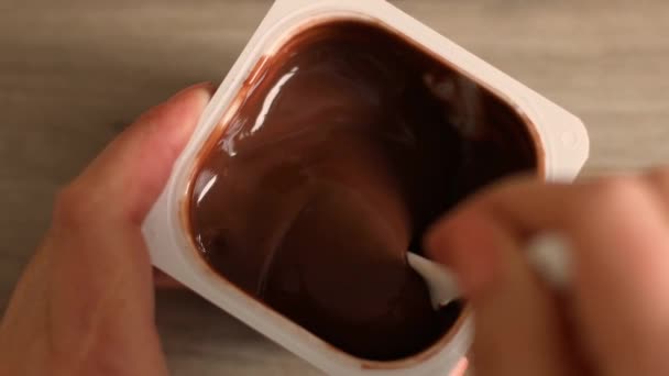 Zbliżenie rąk człowieka wziąć kremowy mus czekoladowy lub pudding z łyżeczką w plastikowym słoiku - Materiał filmowy, wideo