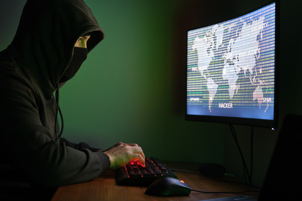 Zamaskowany haker wpisujący komputer do zorganizowania masowego ataku z naruszeniem danych na całym świecie. Pojęcie cyberprzestępczości. - Zdjęcie, obraz