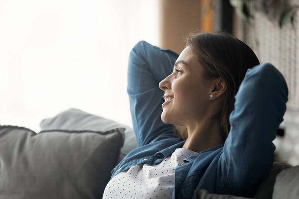 Serene millennial woman relax on sofa with hands over head - Фото, изображение