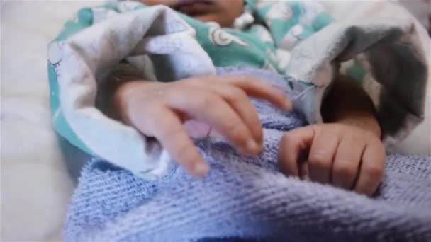 Νεογνό μωρό κινείται τα χέρια και τα πόδια και τα δάχτυλα ενώ κοιμάται. Κλείσε. Όμορφο νεογέννητο αγοράκι σε κοντινή απόσταση ξαπλωμένο στο κρεβάτι, ενώ τυλιγμένο σε κουβέρτα μωρού στο θάλαμο του νοσοκομείου. - Πλάνα, βίντεο