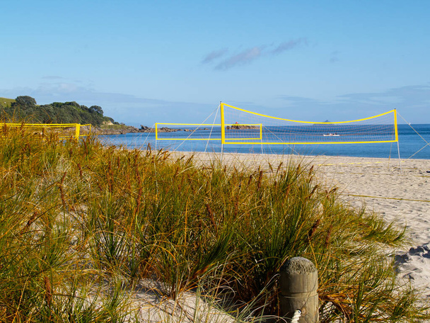 Żółte siatkówki plażowe wzniesione do użytku bez graczy na Mount Maunganui Główna plaża z trawą plażową na pierwszym planie. - Zdjęcie, obraz