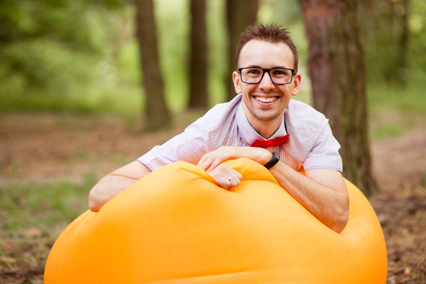 Przystojny młodzieniec w okularach leżący na nadmuchiwanej, żółtej sofie i odpoczywający w parku - Zdjęcie, obraz