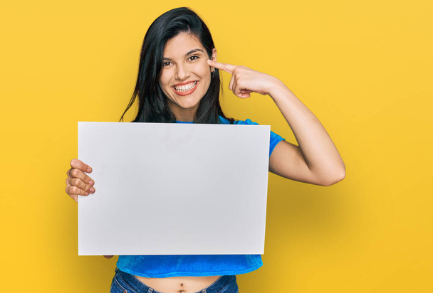 Boş pankart tutan genç İspanyol kadın gülümseyen mutlu ve gururlu birini işaret ediyor.  - Fotoğraf, Görsel