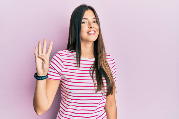 jonge brunette vrouw dragen casual kleding over roze achtergrond tonen en wijzen met vingers nummer vier terwijl glimlachen zelfverzekerd en gelukkig.  - Foto, afbeelding