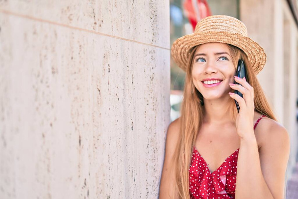 Νεαρή καυκάσια τουρίστρια χαμογελά ευτυχισμένη μιλώντας smartphone ακουμπά στον τοίχο. - Φωτογραφία, εικόνα