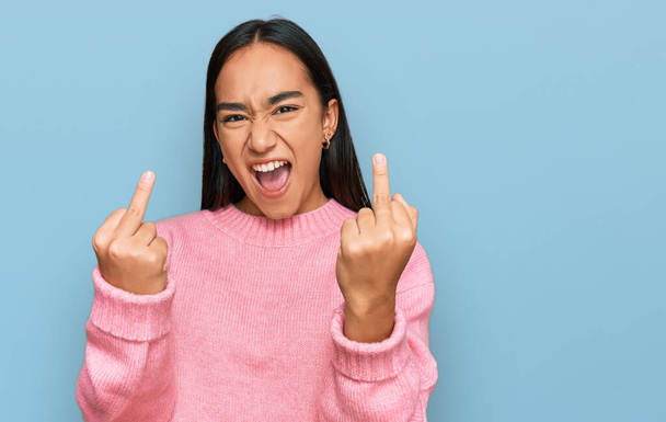 Young asian woman wearing casual winter sweater showing middle finger doing fuck you bad expression, provocation and rude attitude. screaming excited  - Photo, Image