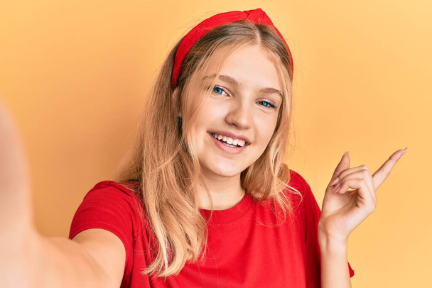 Kaunis nuori valkoihoinen tyttö ottaa selfie valokuva hymyillen onnellinen osoittaa käsi ja sormi sivulle  - Valokuva, kuva