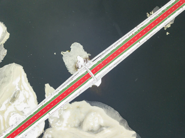 キエフのドニエプル川にかかる赤緑の歩道橋。川の雪のパターン。空中ドローンビュー。冬の雪の朝. - 写真・画像