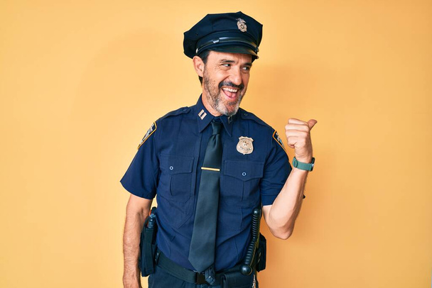 Moyen Age hispanique homme portant uniforme de police souriant avec le visage heureux regardant et pointant vers le côté avec le pouce vers le haut.  - Photo, image