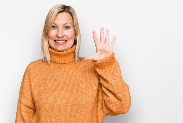 Μέση ηλικία καυκάσια γυναίκα φορώντας casual πουλόβερ χειμώνα δείχνει και δείχνοντας προς τα πάνω με τα δάχτυλα νούμερο πέντε, ενώ χαμογελά αυτοπεποίθηση και χαρούμενος.  - Φωτογραφία, εικόνα