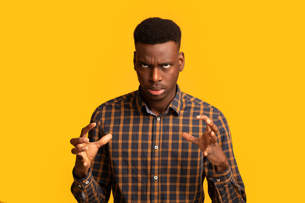 Portrét otráveného černocha v kostkované košili emocionálně gestikulující, žluté pozadí - Fotografie, Obrázek