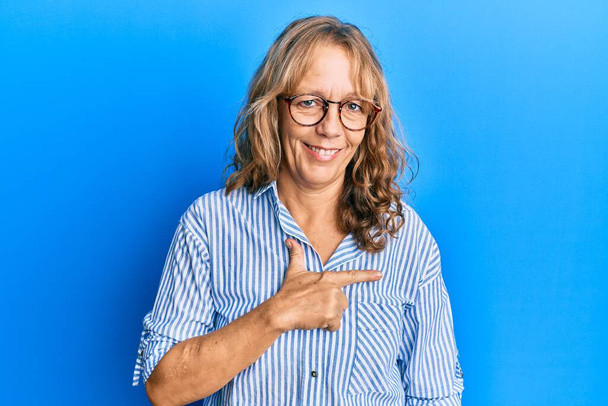 Middle age blonde woman wearing casual clothes and glasses cheerful with a smile on face pointing with hand and finger up to the side with happy and natural expression  - Photo, Image