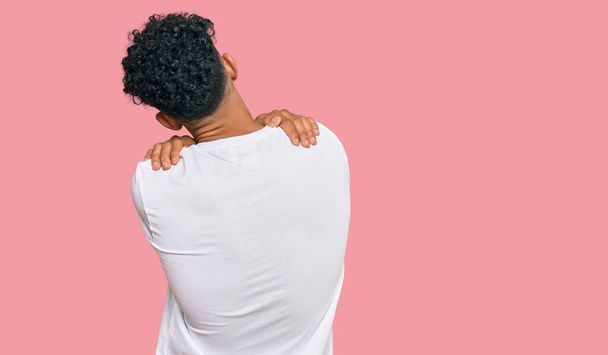 Jeune homme arabe portant un t-shirt blanc décontracté s'embrassant heureux et positif à partir de l'arrière. amour de soi et soins de soi  - Photo, image