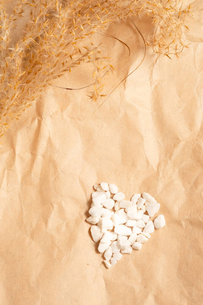 Hierba pampeana y un corazón de piedras blancas sobre un fondo beige artesanal. diseño monocromo - Foto, imagen