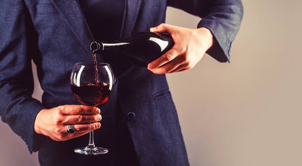 Kelner nalewający czerwone wino do kieliszka. Sommelier człowiek, degustacja, winiarnia, męski winiarz. Czerwone wino nalewa się od butelki do szklanki. - Zdjęcie, obraz