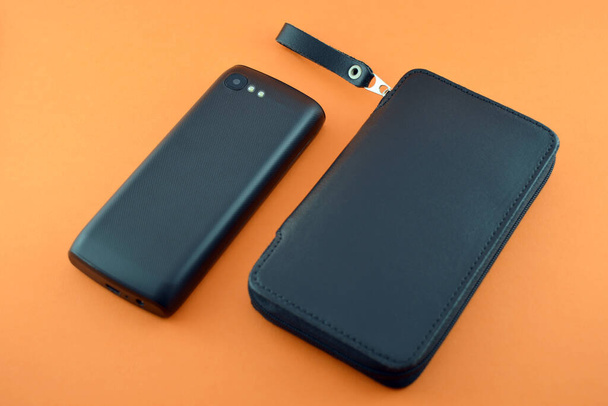 Чорний шкіряний футляр і мобільний телефон на помаранчевому фоні
 - Фото, зображення