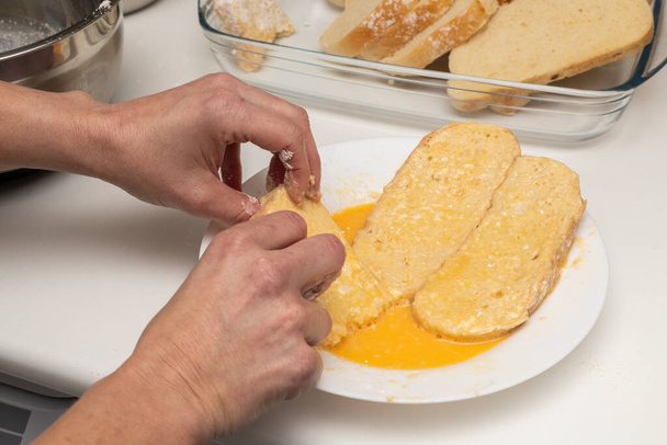 Woman's hands passing bread through egg and flour (Torrijas). Typical Spanish Easter sweet. Traditional home cooking concept. Horizontal photography, close-up and selective focus - Zdjęcie, obraz