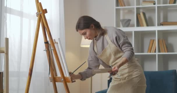geïnspireerd jonge vrouwelijke kunstenaar werkt in huis werkatelier, schilderen op doek, staan in de woonkamer, hobby - Video