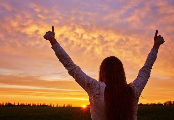 A fiatal nő győzedelmeskedik a gyönyörű naplementével szemben.. - Fotó, kép