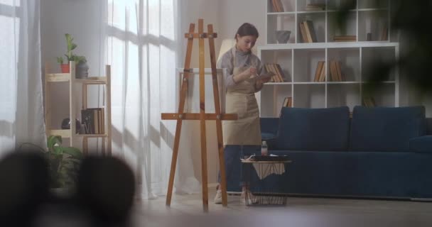 thuiswerkatelier van jonge vrouwelijke schilder, vrouw is kleuren mengen en tekenen op doek in appartement - Video