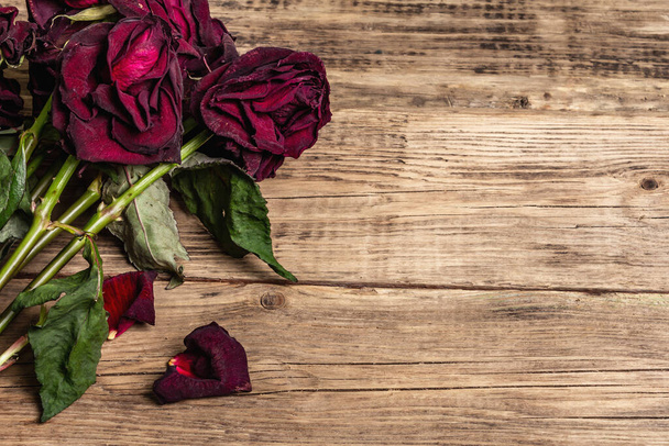 Bouquet of dry burgundy roses. The minimal floral concept on old wooden boards background, place for text, copy space - Photo, Image