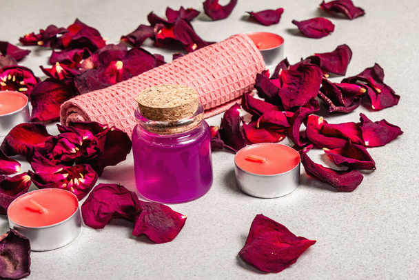 Floral and spa concept with dried roses petals, fragrant candles and soft towel. Natural rose oil, light stone concrete background, close up - Photo, Image