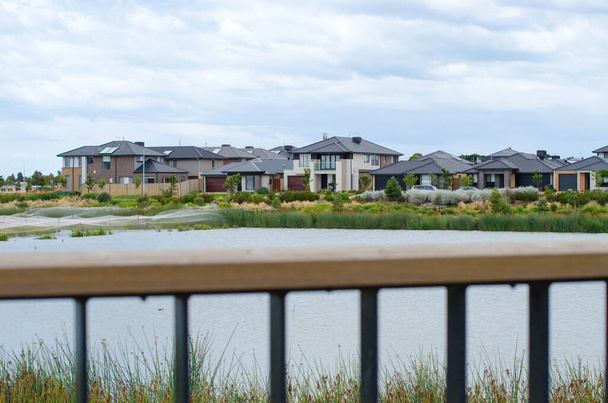 展望台のフェンスの上に湖で近代的な郊外の家の行のビュー。新郊外の不動産開発、住宅市場、オーストラリアの住宅、自然環境の概念. - 写真・画像