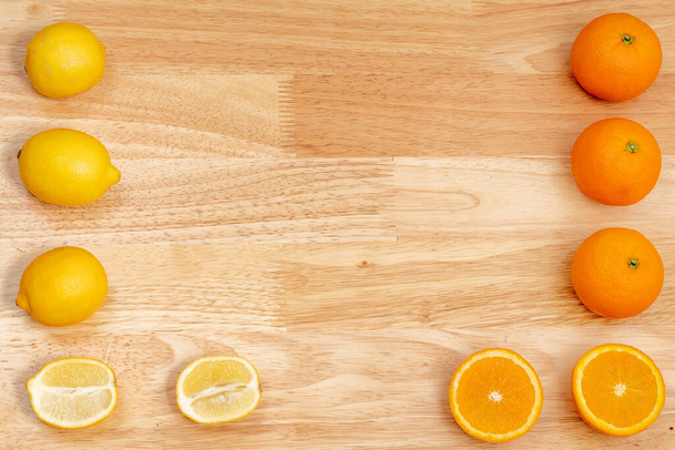 całe cytryny i pokrojone cytryny na drewnianym stole i pomarańcze oraz pokrojone pomarańcze, drewniane dno - Zdjęcie, obraz
