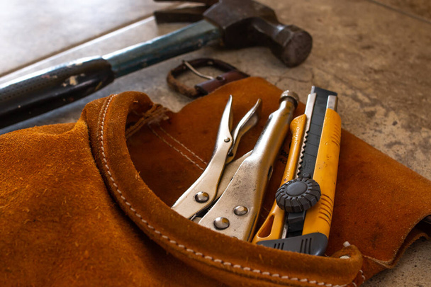 Home improvement tools in a suede tool belt. A multitool, a hammer, and a precision box-cutter knife with yellow edges. - Photo, Image