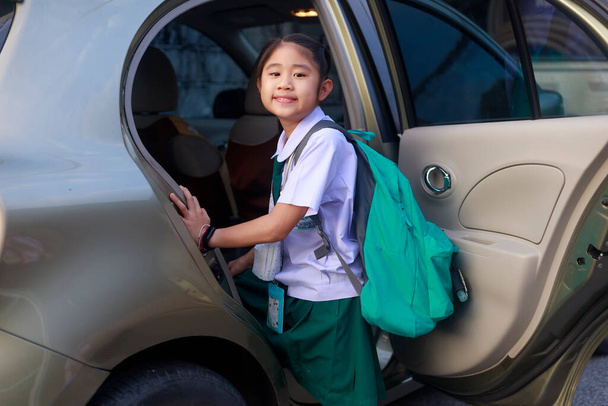 Asyalı liseli kız okul üniforması giyiyor ve sabah okula gitmek için otobüse binerken yeşil bir sırt çantası taşıyor. Mutlu ilkokul çocuğu arabaya bin. Aile araba taşıma konseptinde. - Fotoğraf, Görsel