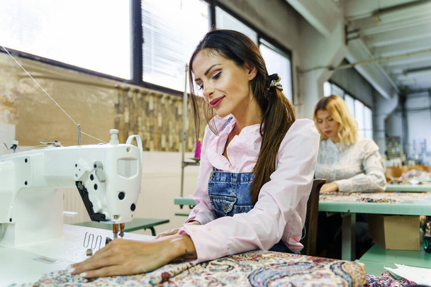 Mooie Kaukasische vrouw werkt aan de naaimachine in de fabriek - jonge vrouwelijke vrouwen op maat maken jurk - ondernemer en fabricage business concept - Foto, afbeelding