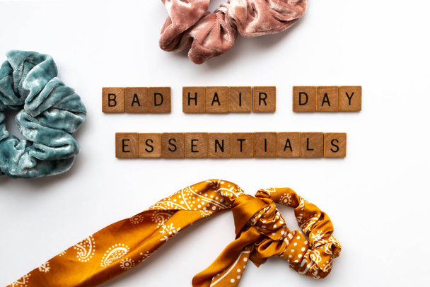 Drewniane litery oznaczają "złe rzeczy niezbędne na dzień włosów" na środku planszy pokrytej aksamitnymi i jedwabnymi gumkami do włosów, Toronto, Ontario, Kanada.  - Zdjęcie, obraz