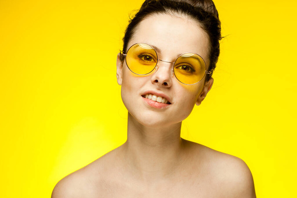 morena con hombros desnudos gafas amarillas sonrisa fondo amarillo - Foto, imagen
