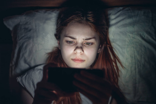 kobieta leży w łóżku przed pójściem do łóżka z telefonem w rękach komunikacji styl życia rekreacji - Zdjęcie, obraz