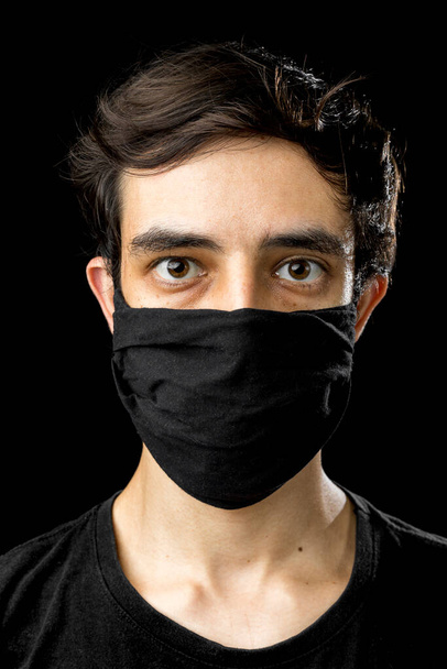 Un joven con una máscara negra. Pandemic coronavirus covid-19 quarantine period concept. Estudio de fondo negro. - Foto, imagen