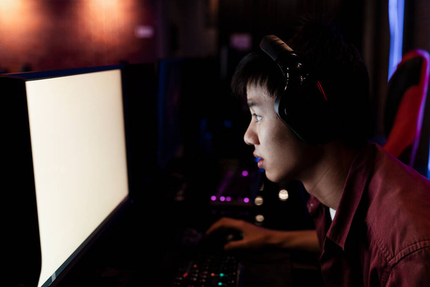 Giocatore asiatico su auricolare guardando troppo da vicino monitor dello schermo. Giocare video gioco su PC. - Foto, immagini