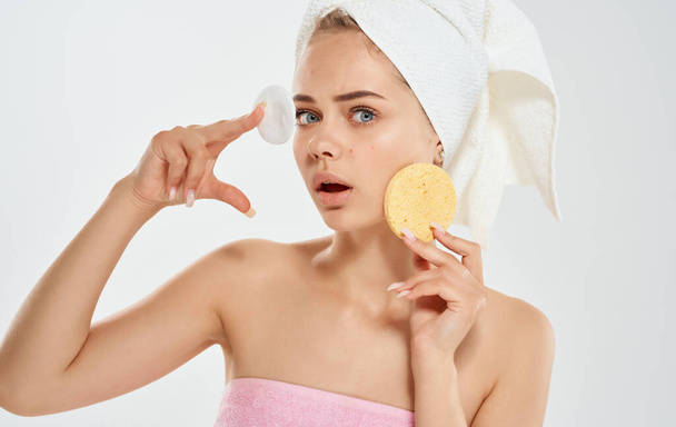 Nainen, jolla on pyyhe päässään, pitää sientä kädessään kosmetologian dermatologisessa mallissa. - Valokuva, kuva
